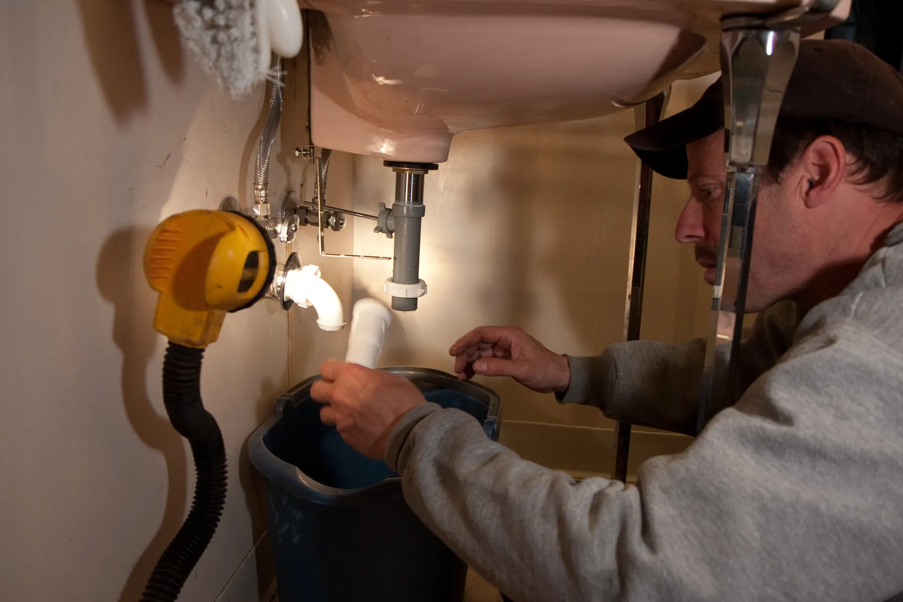 Plumber working under a bathroom sink by the light of a portable work lamp